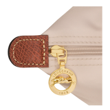 Close-up of a gold zipper pull with 'Longchamp' logo on a beige background
